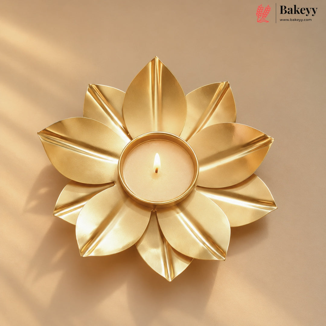 A gold-toned flower-shaped candle holder with a lit tealight candle in the center, set against a warm beige background with soft shadows. The Bakeyy logo is visible in the top right corner.