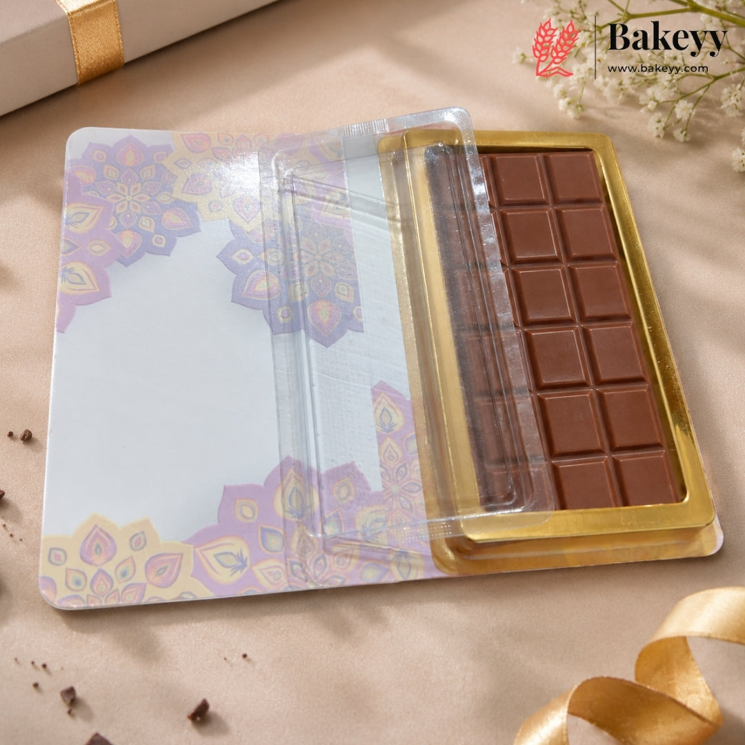 An open decorative chocolate gift box with a gold foil tray holding a chocolate bar, set on a beige surface with floral accents and the Bakeyy logo in the top right.
