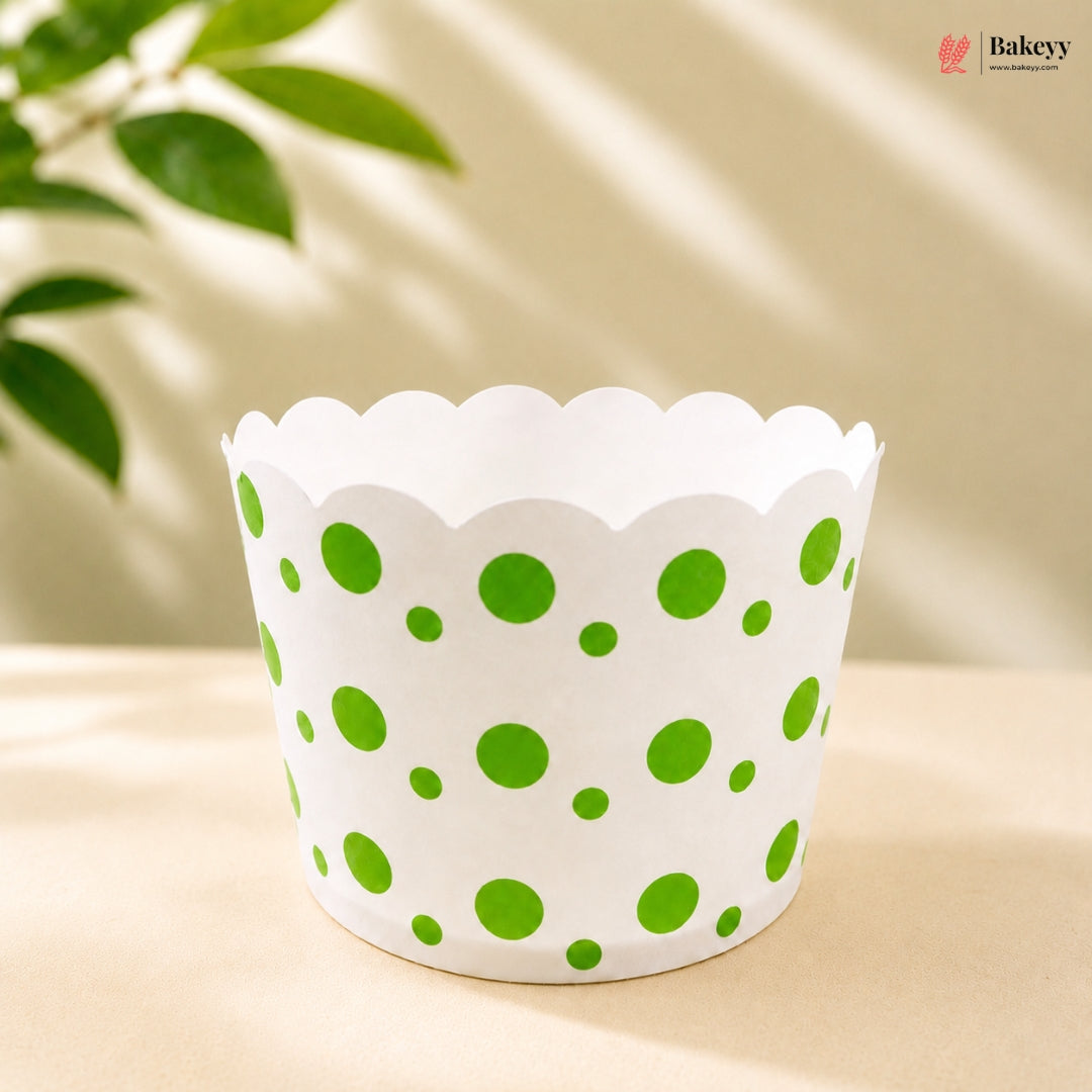 White cupcake liner with green polka dots on a beige surface with a blurred plant background