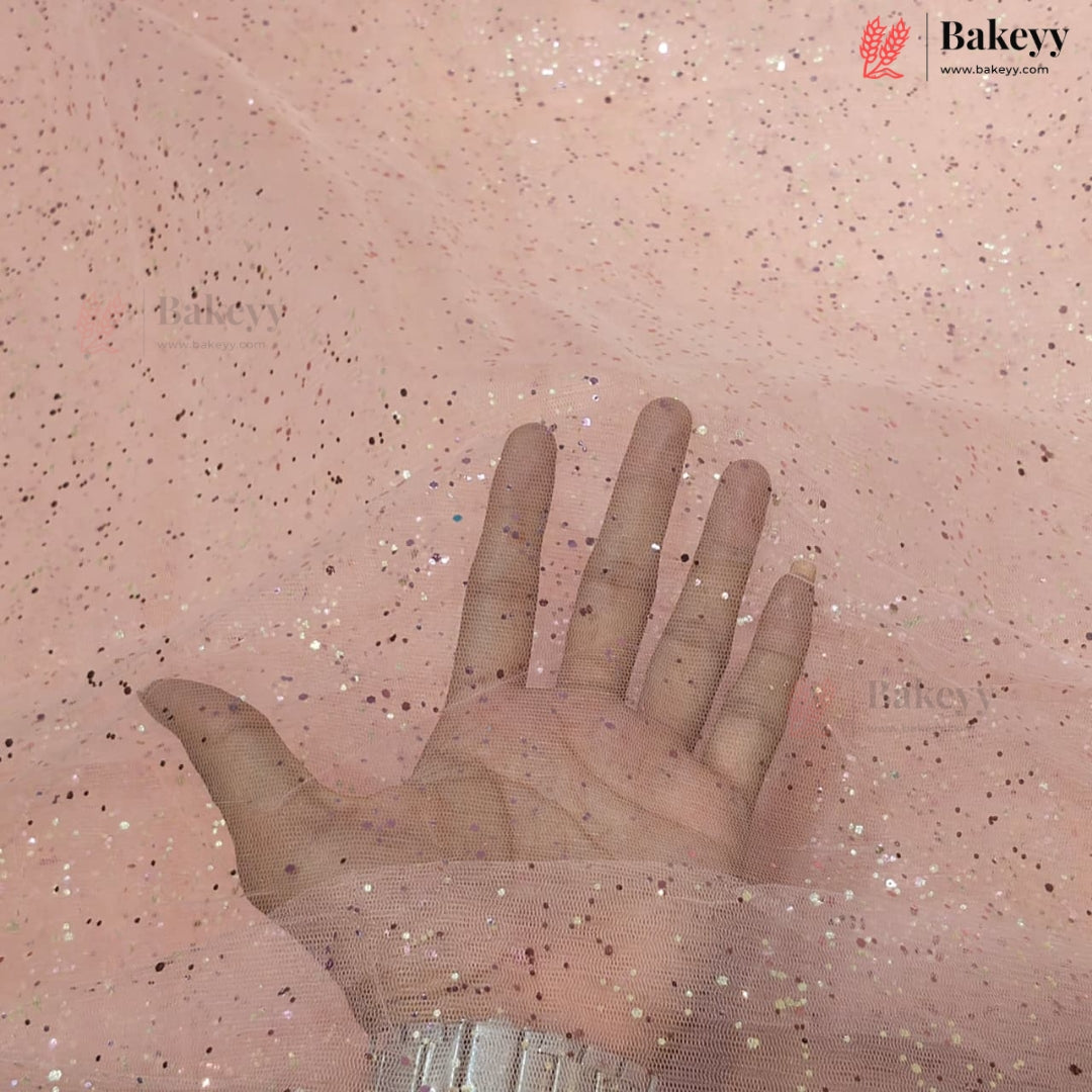 A hand placed over a sheet of pink tulle fabric with scattered glitter, showing the texture and sparkle of the material. The Bakeyy logo is visible in the top right corner.