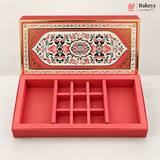 A red rectangular jewelry box with a hinged lid, shown open to reveal a nine-compartment internal organizer. The lid features an ornate, symmetrical floral pattern in red, black, and gold.