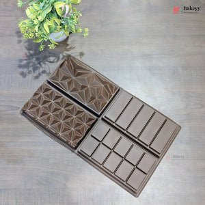 A dark brown silicone baking mold with a geometric star pattern and rectangular sections, displayed on a gray wood-textured surface next to a small green plant.