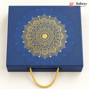 A square blue gift box with a large gold mandala design on the lid and a gold rope handle, photographed on a clean white background. A Bakeyy logo appears in the top right corner.