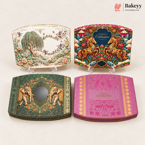 Four decorative rectangular cake boxes displayed on clear stands against a light beige background. The boxes feature intricate traditional-style illustrations: one with a willow tree and birds, one with two horses, one with two elephants, and one pink box with gold text reading 'the TASTE of CELEBRATION'.