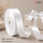 A roll of white satin ribbon with a matching ribbon on a gift box, styled on a beige surface with dried flowers and a gift box in the background. Text at the bottom left reads 'Width : 1 Inch/2.