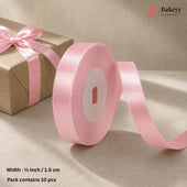 A roll of light pink satin ribbon with a matching bow on a brown kraft paper gift box, set against a neutral beige background. Text at the bottom left specifies the width as 1/2 inch (1.