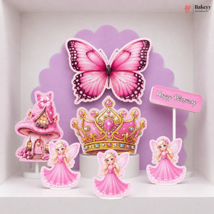 A set of pink fairy-themed birthday cake toppers displayed on a white shelf against a purple scalloped backdrop. The set includes a large pink butterfly, a pink and gold tiara, three fairy figures in pink dresses, a pink castle, and a small 'Happy Birthday' sign.