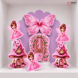 A set of pink fairy-themed party decorations displayed on a white shelf, including a large butterfly, a floral fairy door, two mushroom houses, and two fairy cutouts.