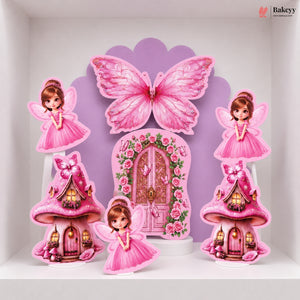 A set of pink fairy-themed party decorations displayed on a white shelf, including a large butterfly, a floral fairy door, two mushroom houses, and two fairy cutouts.