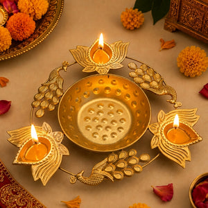 A decorative brass Diwali oil lamp holder with a central bowl and three petal-shaped candle holders, arranged on a beige surface with marigold flowers and petals around it.