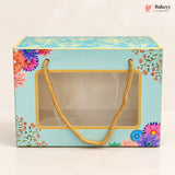 A rectangular bakery gift box with a light blue background, multicolor floral illustrations, and a clear front window holding a gold chain handle, photographed on a clean white background. The Bakeey logo appears in the top right corner.