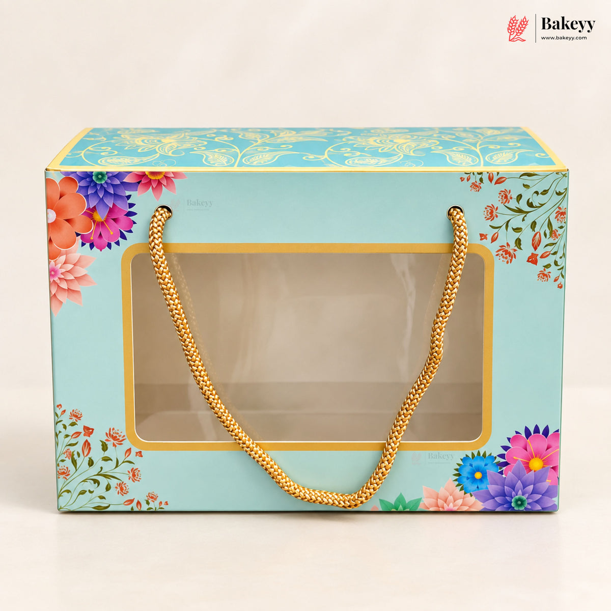 A rectangular bakery gift box with a light blue background, multicolor floral illustrations, and a clear front window holding a gold chain handle, photographed on a clean white background. The Bakeey logo appears in the top right corner.