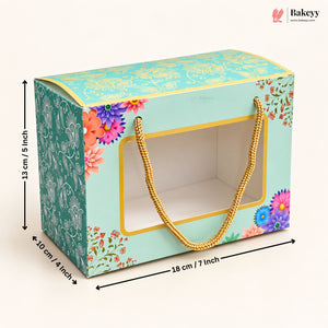 A decorative rectangular gift box with a clear front window and gold rope handles, shown with dimension arrows and labels indicating 18 cm length, 10 cm width, and 13 cm height on a light beige background. The Bakeyy logo appears in the top right corner.