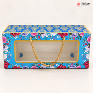 A rectangular bakery gift box with a clear front window, decorated with a bright blue floral pattern and gold handles, shown on a plain light background.