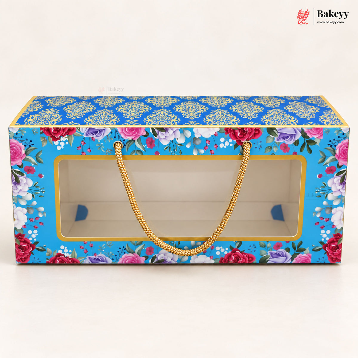 A rectangular bakery gift box with a clear front window, decorated with a bright blue floral pattern and gold handles, shown on a plain light background.