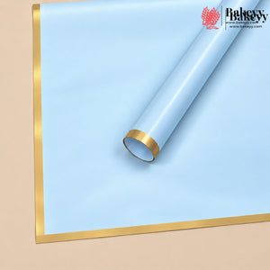 A roll of light blue bakery backdrop paper with metallic gold borders, shown partially unrolled on a beige background. The Bakeey brand logo is visible in the top right corner.