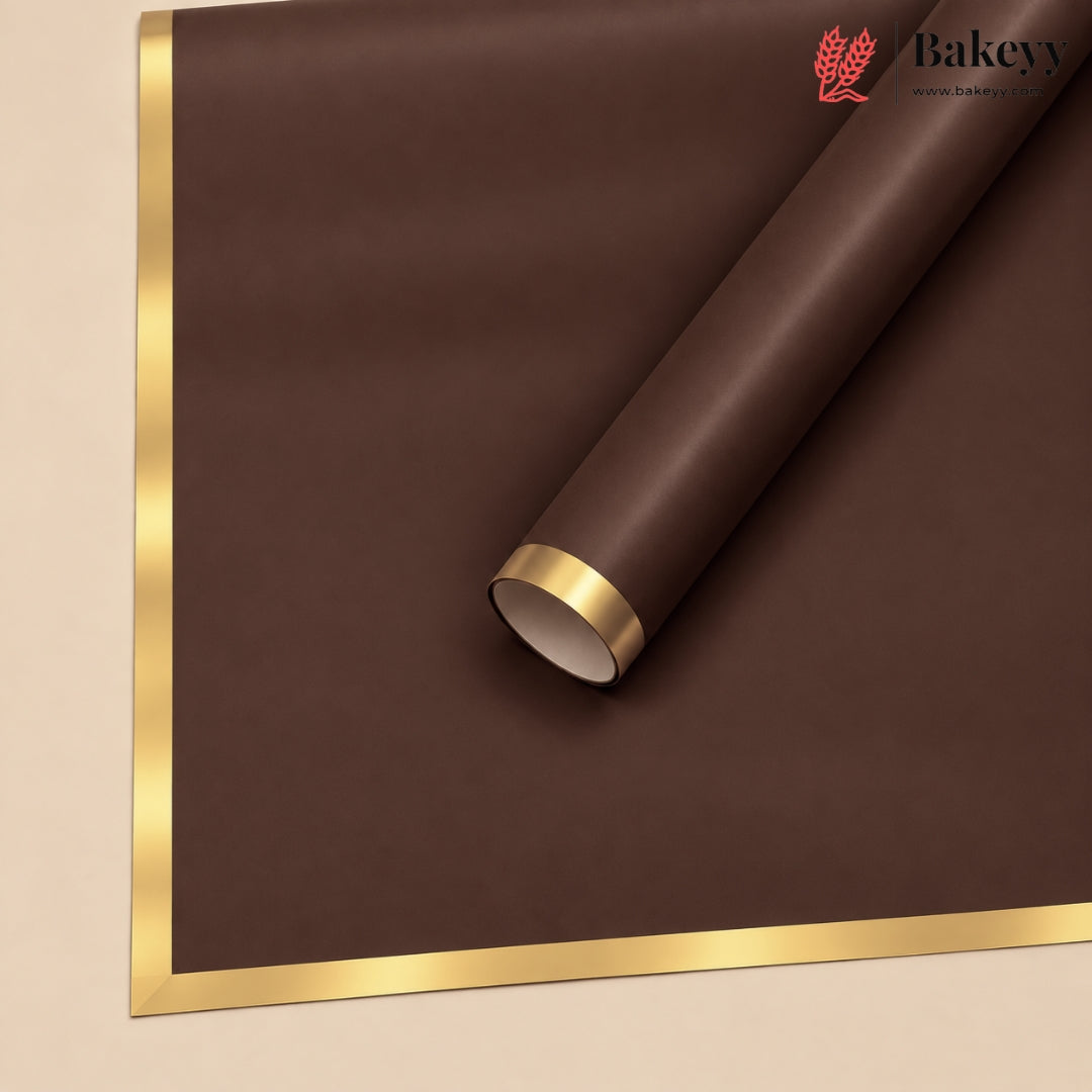 A roll of dark brown bakery wrapping paper or mat with a shiny gold metallic border, shown partially unrolled on a light beige background. A Bakey logo is visible in the top right corner.