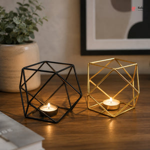 Geometric candle holders on a wooden surface with a plant and framed picture in the background.