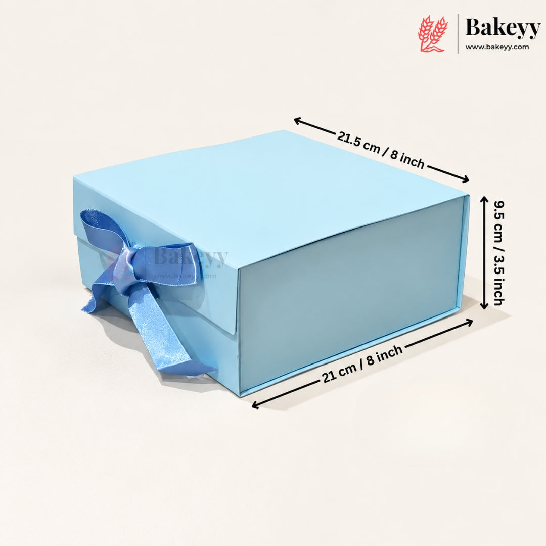 A light blue rectangular gift box with a matching blue ribbon bow on the side, shown on a plain light beige background with dimension arrows and text indicating measurements of 21.5 cm / 8 inch, 9.