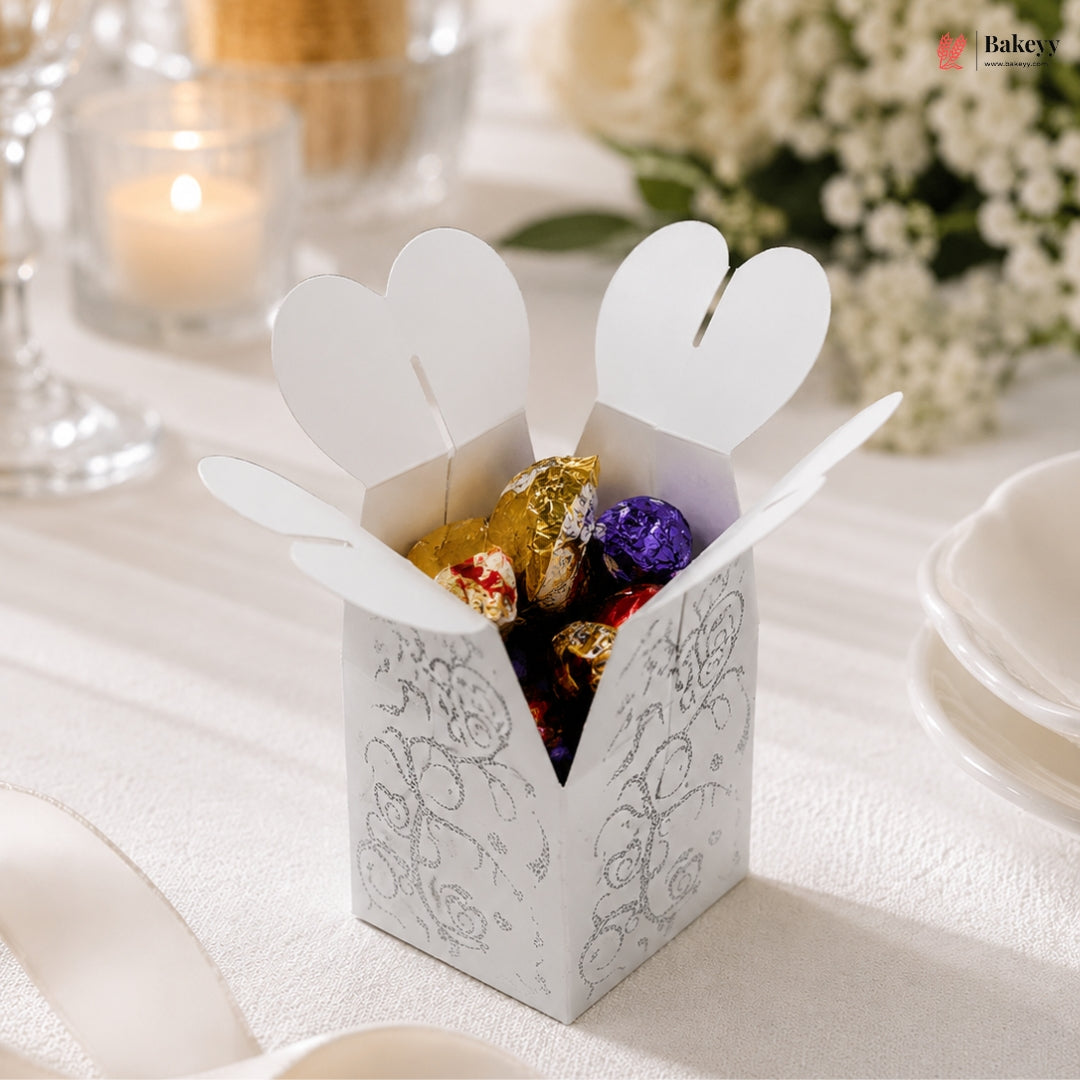 White decorative box with heart-shaped flaps containing colorful candies on a white surface.