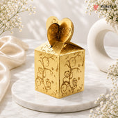 Gold decorative box with heart design on top, placed on a marble surface with white flowers.