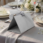 Gray gift box with a ribbon on a table setting with plates, silverware, and flowers.