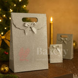 Silver gift bag with a bow on a wooden surface with Christmas decorations.