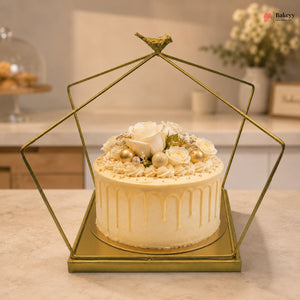 Decorative cake with white flowers and gold accents in a geometric gold stand on a countertop.