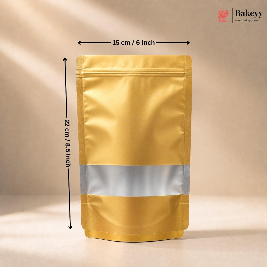 A gold stand-up pouch packaging bag with a silver reflective band around the middle, shown with dimension arrows indicating 15 cm width and 22 cm height on a beige background. The Bakeyy logo is in the top right corner.