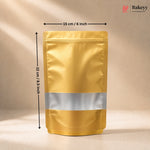 A gold stand-up pouch packaging bag with a silver reflective band around the middle, shown with dimension arrows indicating 15 cm width and 22 cm height on a beige background. The Bakeyy logo is in the top right corner.