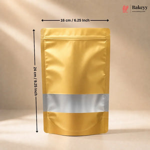 A metallic gold stand-up pouch bag with a reflective silver band across the middle, shown with dimension arrows indicating 16 cm by 24 cm on a beige studio background. A Bakeyy logo appears in the top right.