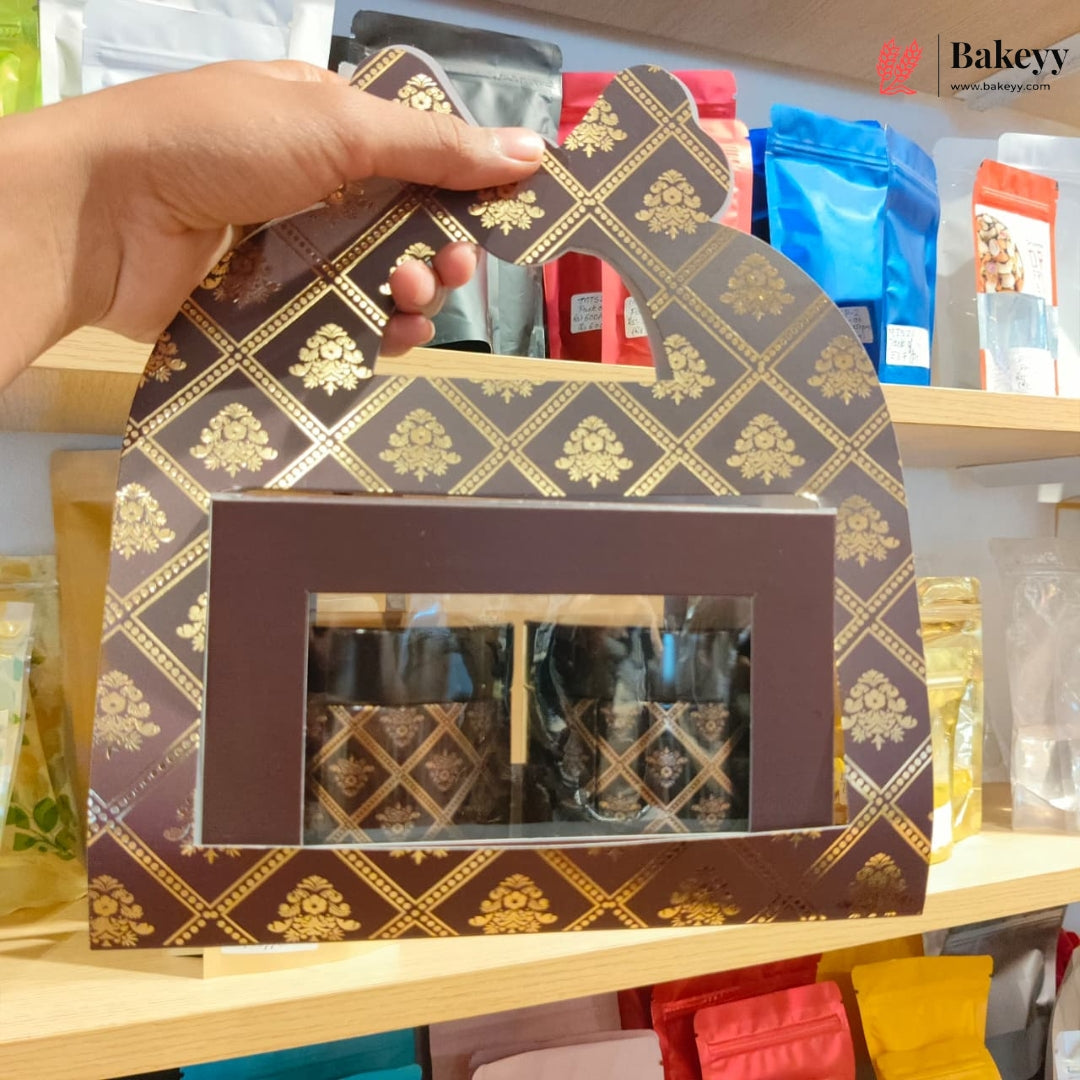 A hand holds a decorative brown and gold patterned gift box with a clear window displaying packaged items inside, set against a shelf background with colorful pouches.