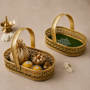 Two ornate gold-toned metal baskets with arched handles are arranged on a beige surface. One basket is filled with sweets, nuts, and a small fabric pouch, while the other is empty and shows a green insert with white decorative text.