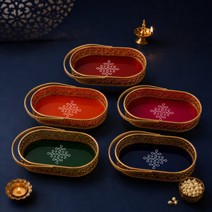Six oval decorative trays with gold-toned filigree borders and colorful interiors are arranged on a dark navy surface. The trays are in red, orange, magenta, green, and navy blue, each with a white geometric motif in the center.