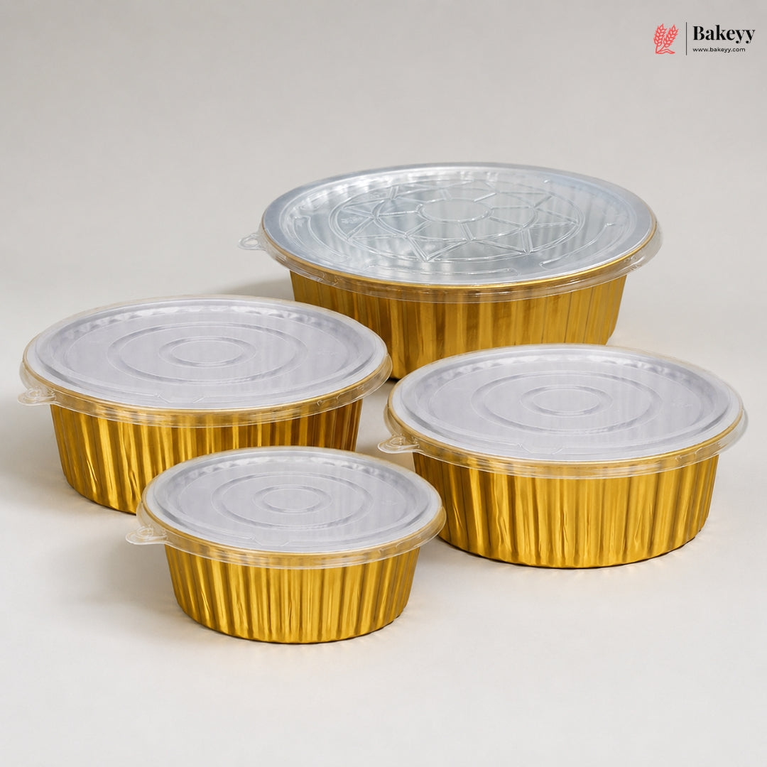 Four round gold foil take-out containers with clear plastic lids, shown in different sizes on a light gray background. A Bakeyy logo is visible in the top right corner.