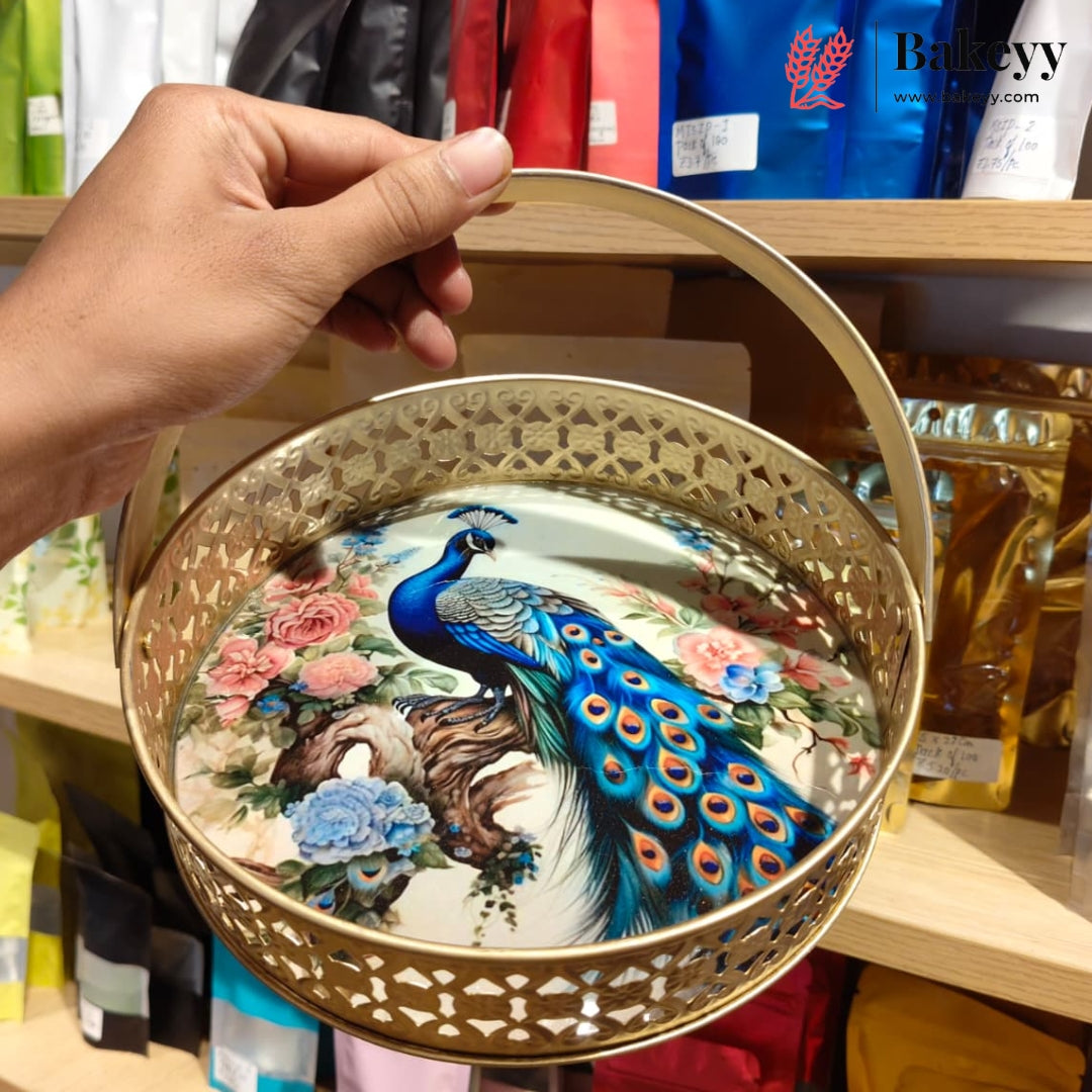 A hand holds a round gold-tone metal basket with a cutout pattern and a handle, featuring a printed peacock and floral design on the inside. The background shows a retail shelf with various colorful items.