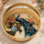 Round gold metal serving basket with a cutout pattern and a handle, featuring a colorful printed peacock and floral design on the inside, shown on a light beige surface with soft shadows.