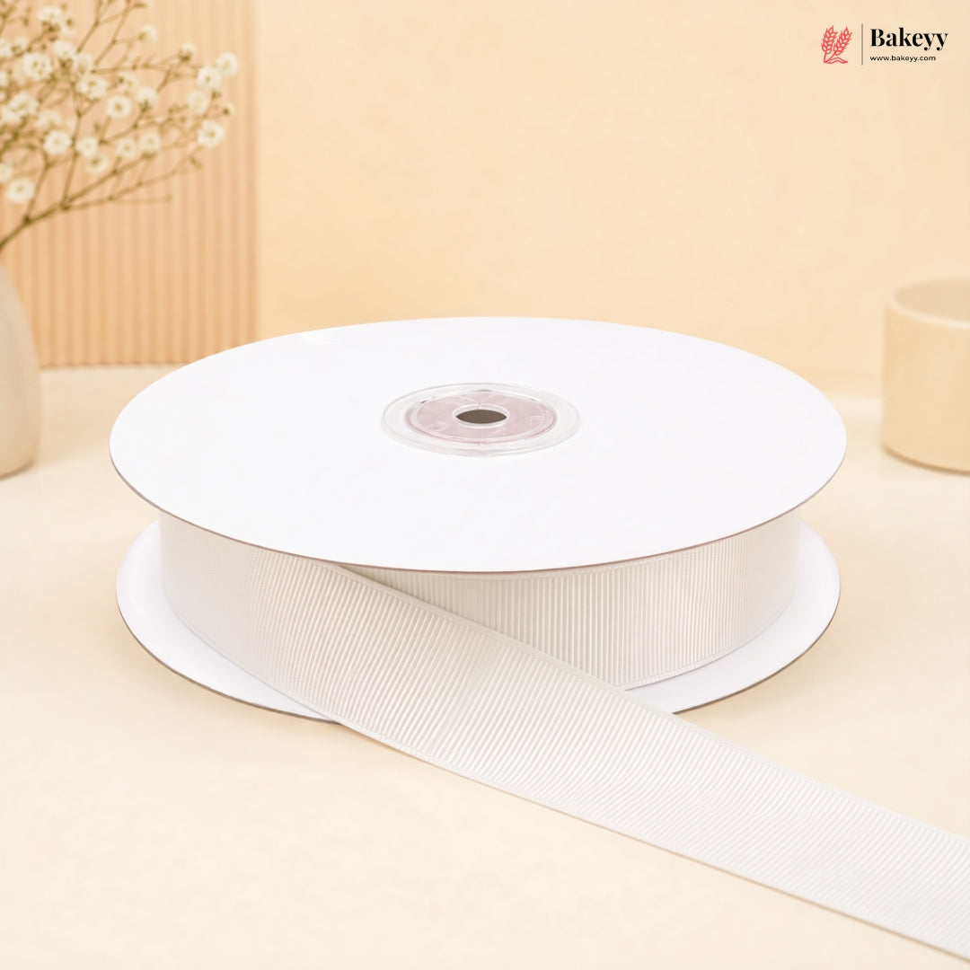 A spool of white grosgrain ribbon with one end unspooled, set against a warm beige background with decorative dried flowers.