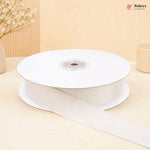 A spool of white grosgrain ribbon with one end unspooled, set against a warm beige background with decorative dried flowers.