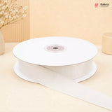 A spool of white grosgrain ribbon with one end unspooled, set against a warm beige background with decorative dried flowers.