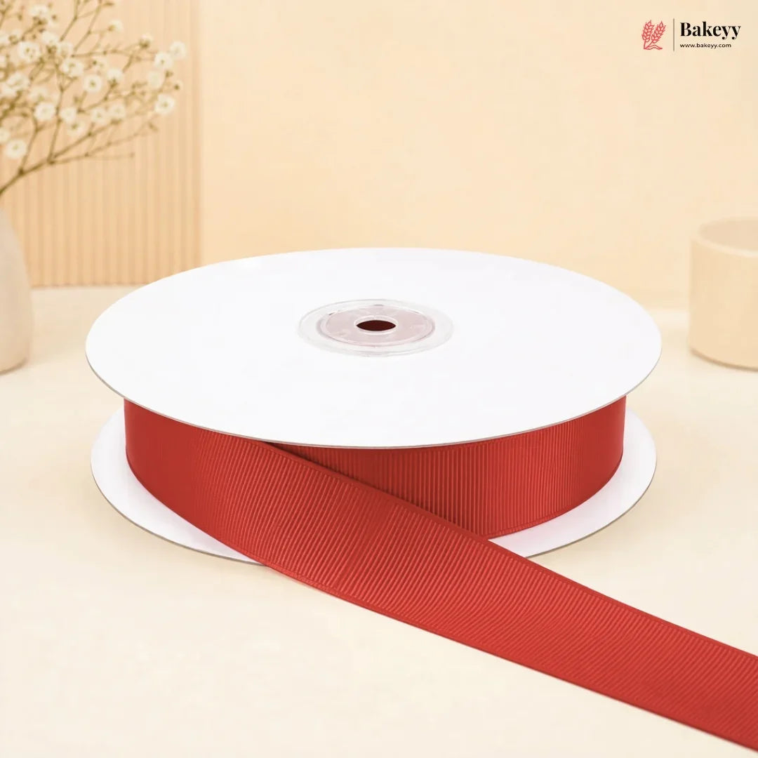 A spool of red grosgrain ribbon with one end unspooled, set against a warm beige background with decorative dried flowers.