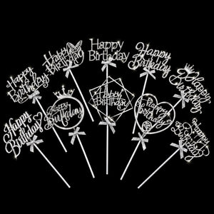 A set of ten silver acrylic birthday cake toppers with 'Happy Birthday' designs, including script, hearts, crowns, butterflies, and geometric frames, arranged in a fan shape on a solid black background.