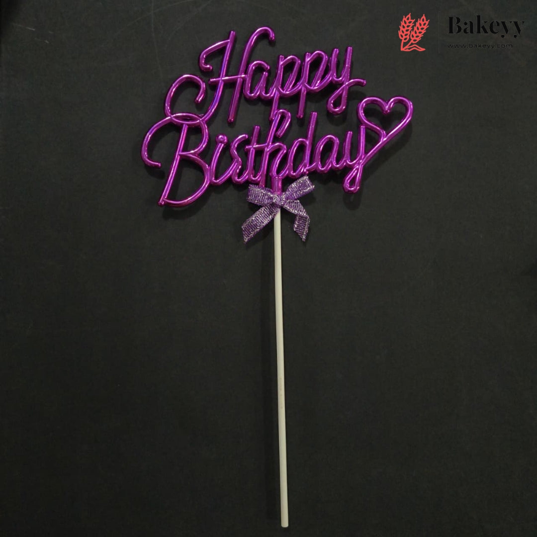 A purple glittery 'Happy Birthday' cake topper with a small bow on a stick, set against a dark background. A Bakeyy logo is visible in the top right corner.