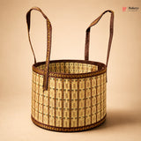 A round woven basket with two long handles, made from natural straw and dark brown trim, shown on a solid beige background. A Bakeey logo is visible in the top right corner.