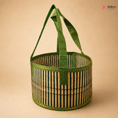 A round woven bamboo basket with green fabric handles, featuring vertical black and natural bamboo stripes with green braided trim, set against a solid beige background.