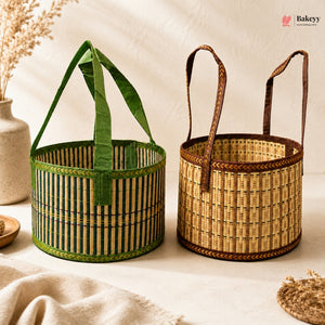 Two woven bamboo baskets with fabric handles, one green and one natural tan, displayed on a neutral cream surface with a beige ceramic vase in the background.