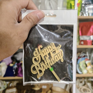 Gold 'Happy Birthday' cake topper in a clear plastic bag held by a hand.