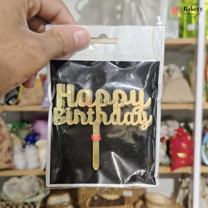 Gold 'Happy Birthday' cake topper in clear packaging held by a hand, with a blurred background.