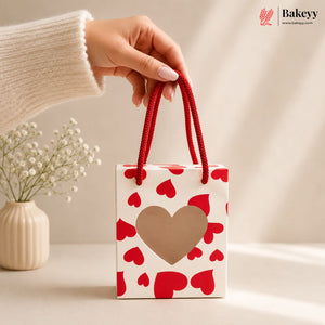 Hand holding a small gift bag with red hearts and a beige heart on a neutral background, featuring the Bakey brand.