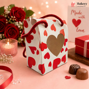 Gift bag with heart design on a pink surface with chocolates and flowers